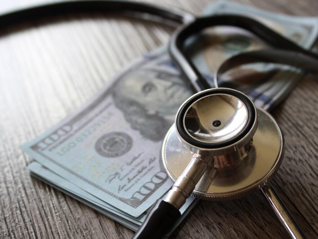Stethoscope and money on wooden table. Healthcare, medical treatment cost and medicine concept.